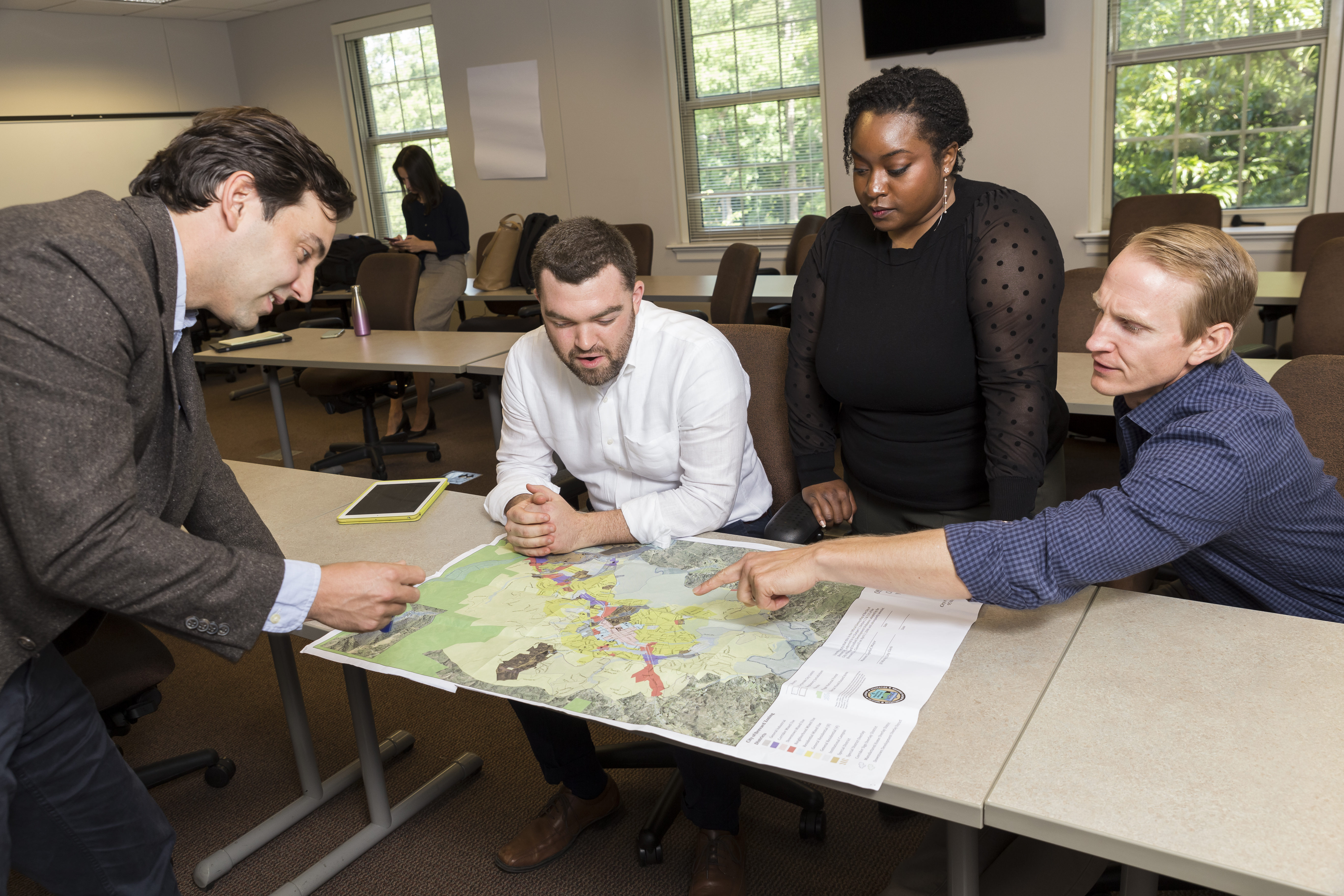 Four people stand around a table gesturing at a map